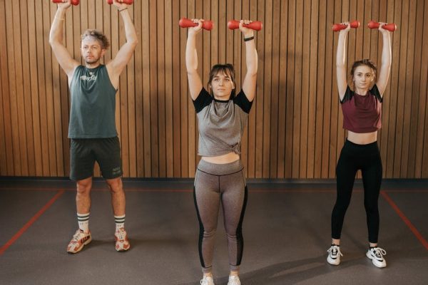 Three adults exercising with dumbbells in a gym setting, promoting fitness and healthy lifestyle.