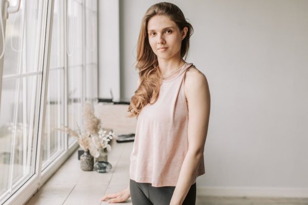 A young woman stands next to a sunlit windowsill, creating a tranquil ambiance.